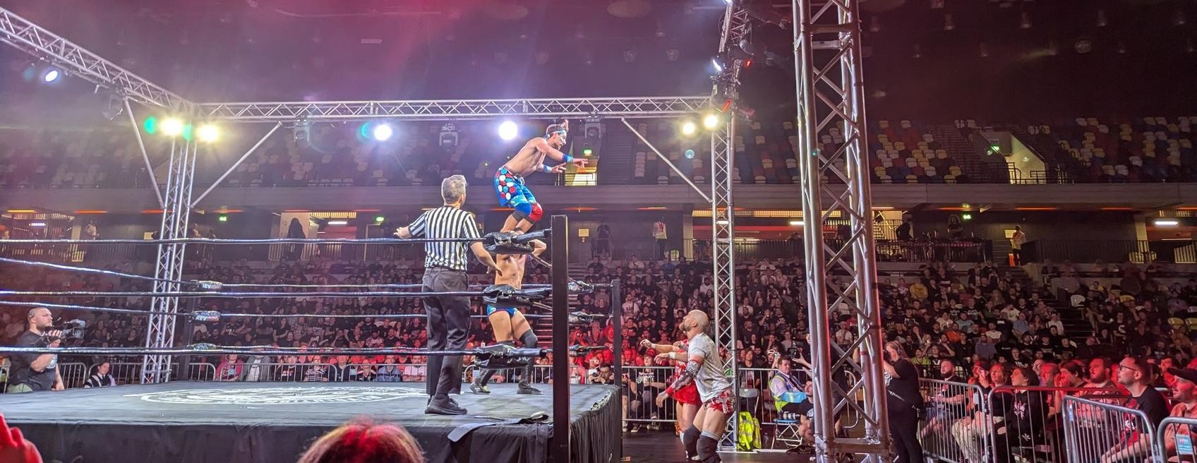 Chuck Mambo stands on TK Cooper's shoulders, preparing to leap over the top rope onto the Grizzled Young Veterans