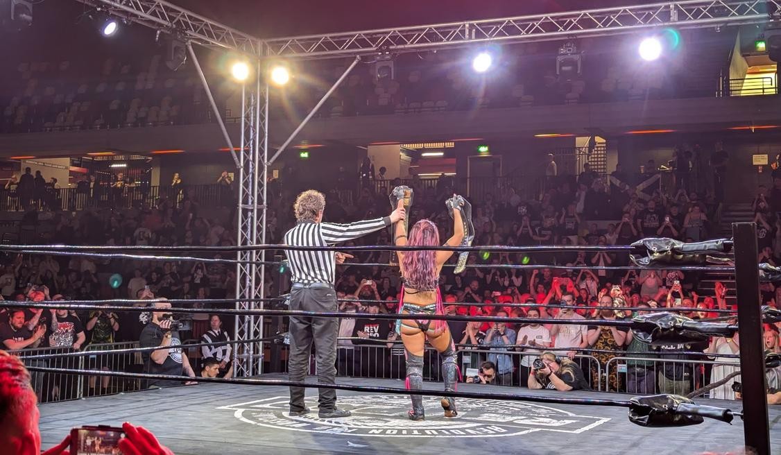 The referee raises Mina Shirakawa's hand in victory as she holds both titles