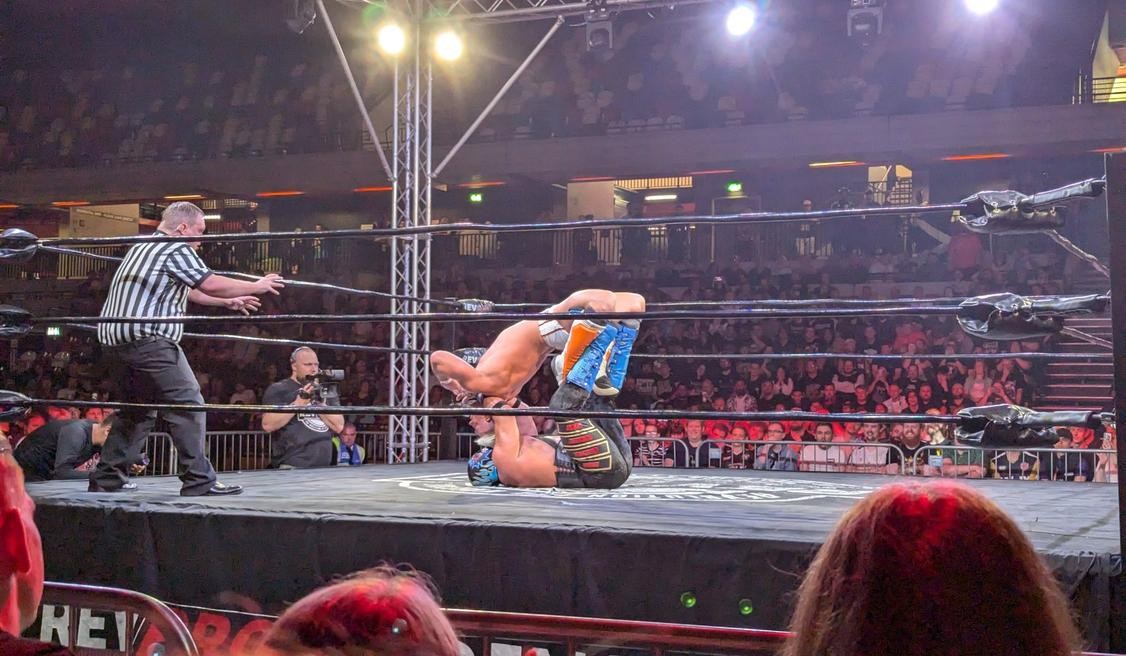 The referee watches as Zack Sabre Jr. applies a Mexican surfboard to Hechicero